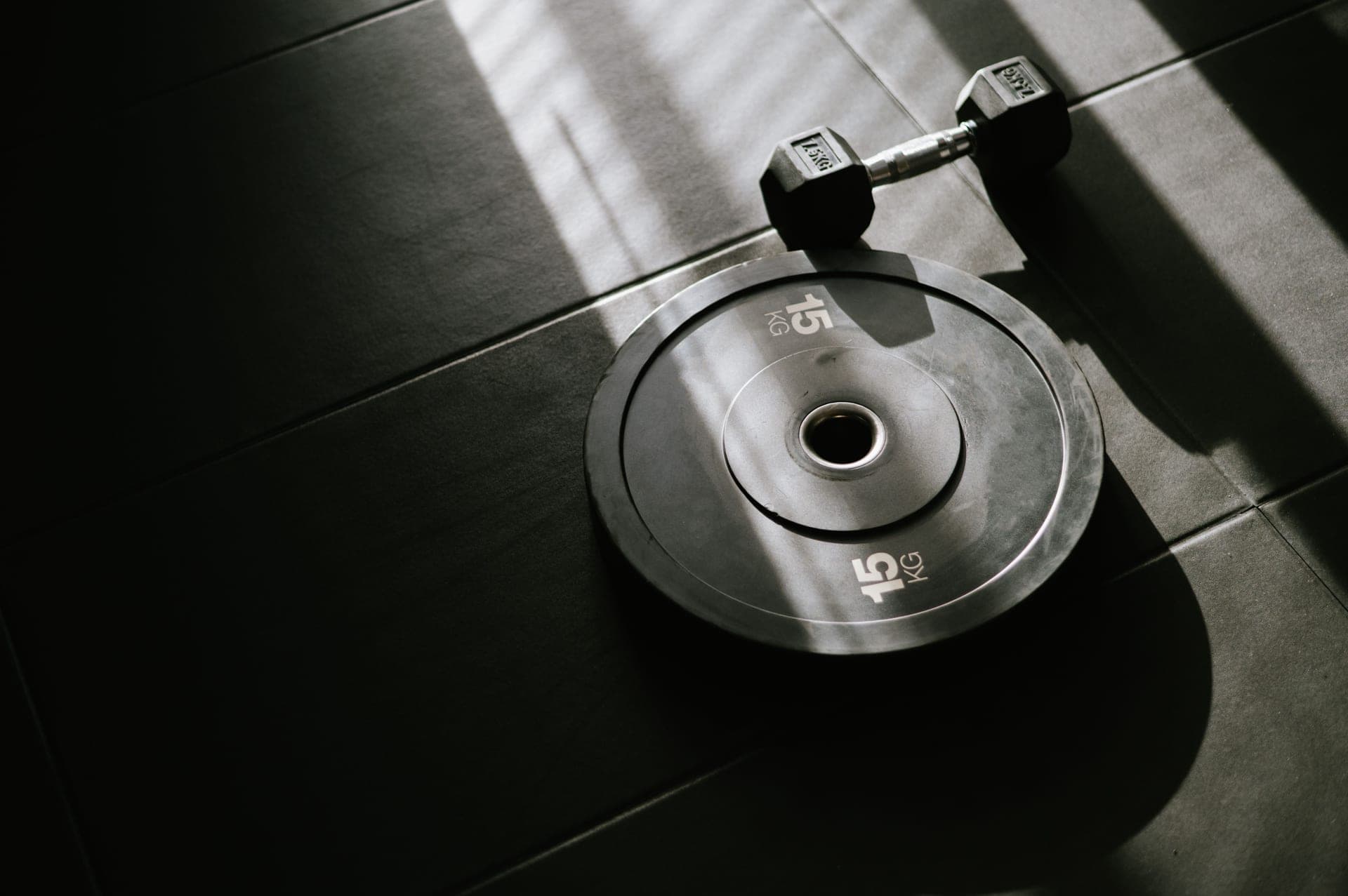 Adjustable dumbbells and a loaded barbell on rubber gym flooring